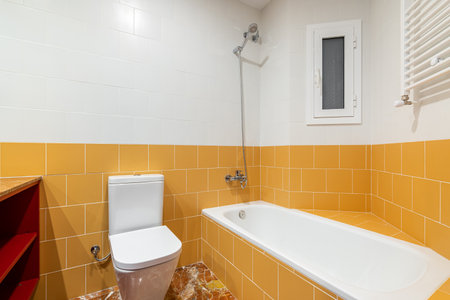 Modern brightly lit bathroom in flashy orange and white with a new white bathtub and toilet. Bathroom has a small plastic window for fresh air. Abstract pattern room tiled floor.の写真素材