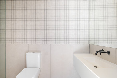 Modern minimalist bathroom interior design with white sink, toilet, beige tiles, and large mirror.の写真素材