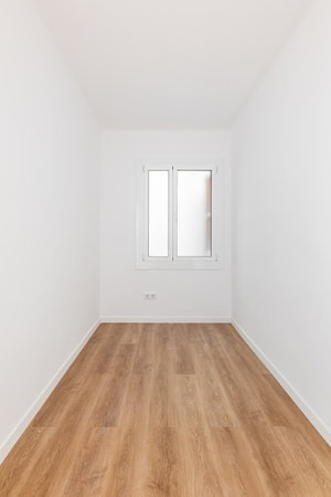 Long narrow rectangular room with white walls and wooden parquet, well lit by daylight from frosted...
