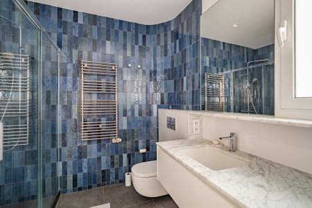Bathroom with marble tiles on walls in deep blue in two monochrome shades. Square sink with marble...