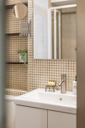 Close-up fragment of stylish bathroom with beige mosaic tiles, mirror, sink and shelves for things. Concept of a comfortable and practical bathroom in a small apartmentの写真素材