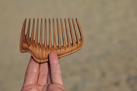 A hand holding natural wooden comb made of pear tree for scalp massage and aroma combing