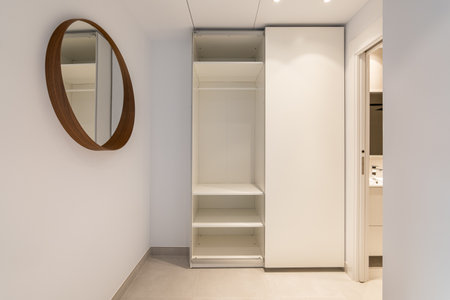 Narrow room with mirror and an open wardrobe with an entrance to the bathroom in light beige tones. Concept of comfortable compact apartment in a new building. Copyspaceの写真素材