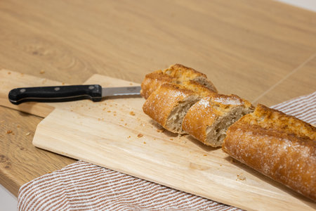 Sliced French bread with knife on cutting board on kitchen towel