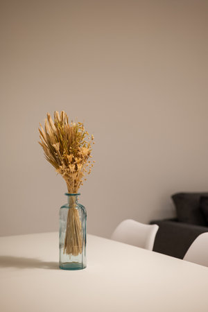 Side angle of dining table with white chairs and blue vase centerpiece holding dried floral bouquetの写真素材