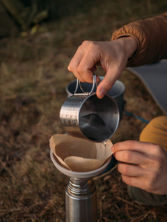 Close view of outdoor coffee brewing with metal cup pouring into paper filter funnel