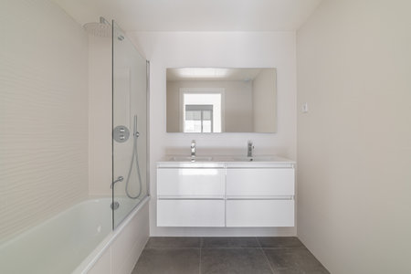 Modern bathroom with a white bathtub, sleek vanity, and large mirror. Neutral color scheme with...