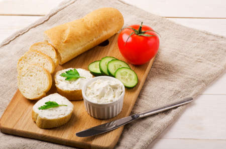 Crunchy baguette slices with cream cheese and vegetables on a cutting boardの写真素材