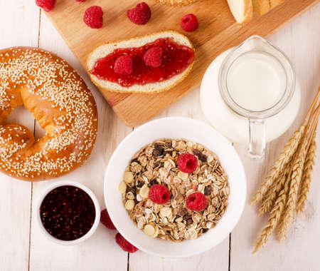 Healthy dietary breakfast with muesli, milk, fresh raspberries, jam and bun on a wooden table, view from aboveの写真素材