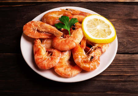 Prepared shrimp with lemon and parsley on a white plate on wooden background の写真素材