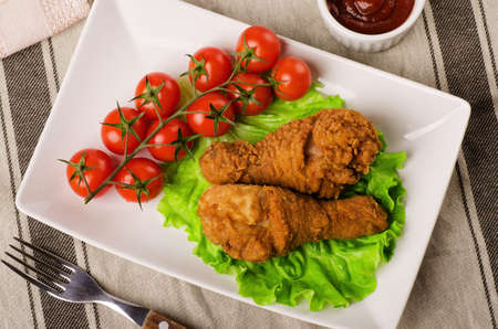 Breaded chicken legs with tomatoes and salad on a white plateの写真素材