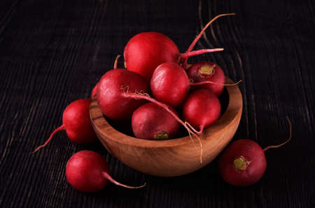 Organic red radish on dark in wood bowl wooden backgroundの写真素材