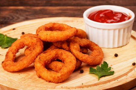 Homemade breaded crunchy fried onion rings with ketchup on cutting boardの写真素材