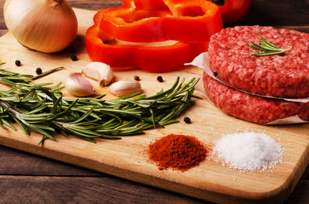 Raw ground beef burgers cutlets with red onion, garlic, olive and red pepper oil to prepare for frying in oven, close-upの写真素材