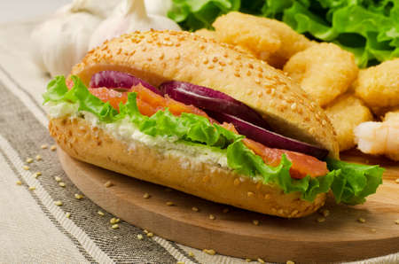 Sandwich with cereals bread, salmon, salad and onion on a cutting board