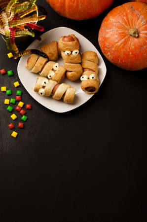 Scary sausage mummies in dough with funny eyes on table and spase for text. Halloween food.の写真素材