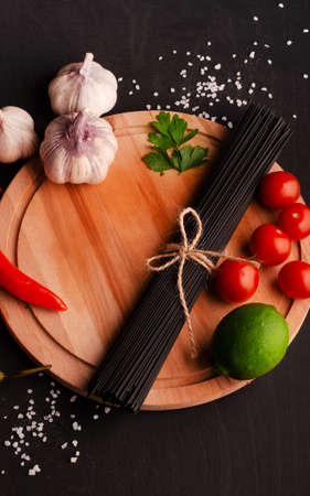 Black spaghetti with ingredients for cooking pasta on a black background