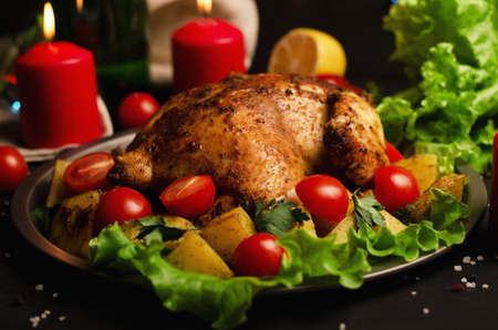Christmas dish. Xmas baked whole chicken with tomatoes and potatoes close-up on a plate on a table with candleの写真素材