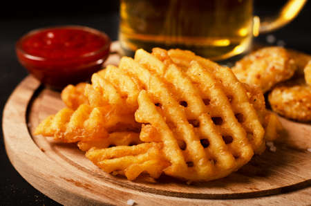 Crispy potato waffles fries, wavy, crinkle cut, criss cross cries with on a cutting board