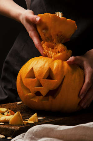 Hands cutting, carving pumpkin into jack-o-lanterns for halloween close up. Smiling halloween pumpkin holiday decoration.