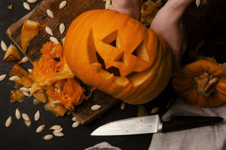Hands cutting, carving pumpkin into jack-o-lanterns for halloween close up. Smiling halloween pumpkin holiday decoration.の写真素材