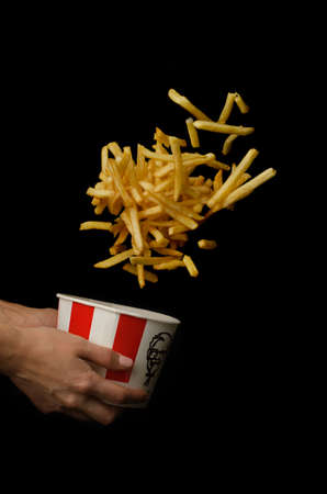 Moscow, Russia - June 16, 2020: KFC bucket (Kentucky Fried Chicken) with flying french fries in female hands, fast food. On a black background.のeditorial素材