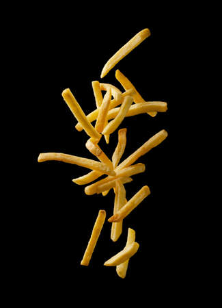 French fries - fried potatoes flying. Fly fastfood isolated on black background.