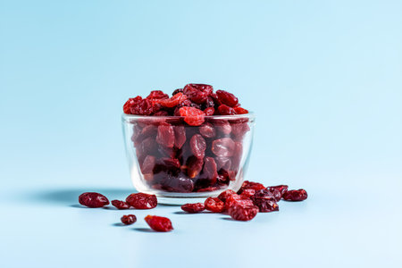 Dried cranberries in a glass bowl on a blue background.の素材