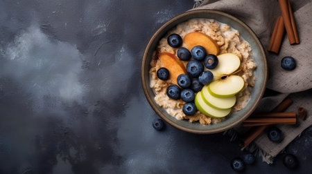 Oatmeal with blueberries and apple in bowl on dark background. Top view with copy spaceの素材
