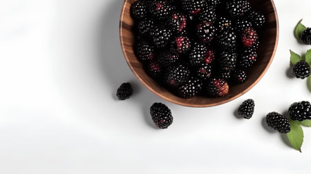 Blackberries in a wooden bowl with leaves on a white background.の素材