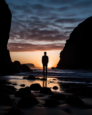 Silhouette of a man standing on the beach at sunset.の素材