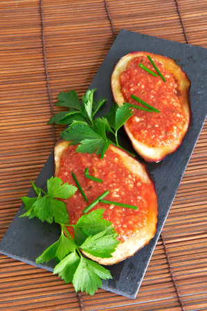 Grilled slices of eggplant on a slate tray woth tomato, onion, chive and parsleyの写真素材