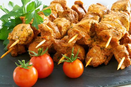 Meat brochettes on a black slate tray with some tomatoes and parsleyの写真素材