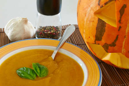 A bowl of pumpkin soup with a couple of basil leaves, pepper, garlic and a Halloween pumpkinの写真素材