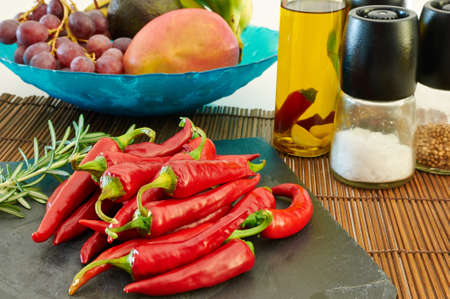 Some red hot chili peppers on a slate tray with fruit and other ingredients on the backgroundの写真素材