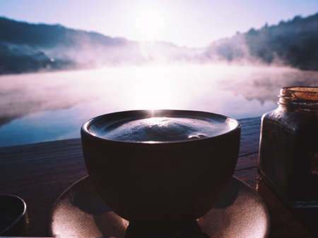 Silhouette a cup of coffee near lake in the morningの写真素材