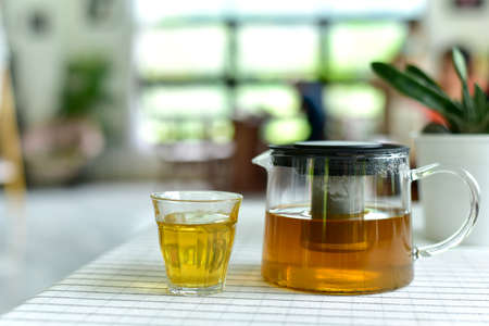 Cup of tea and glass jars on the table covered with white cloth. Hot Tea  water is poured from the kettle into a cup with tea leaves. Pour black tea into a glass cup on table in cafe. selected focusの写真素材