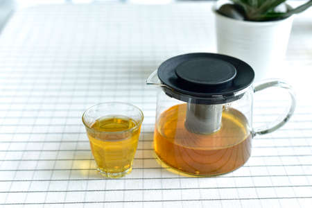 Cup of tea and glass jars on the table covered with white cloth. Hot Tea  water is poured from the kettle into a cup with tea leaves. Pour black tea into a glass cup on table in cafe. selected focusの写真素材