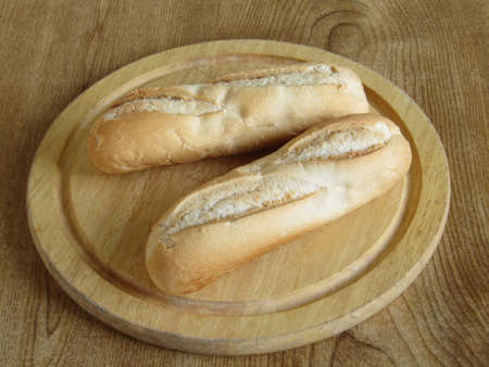 2 breadrolls on a breadboard left on a tableの写真素材