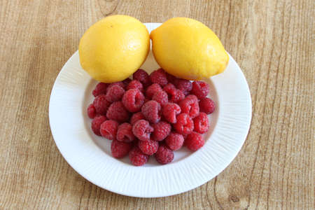 Some raspberries and lemons displayed on a white plateの写真素材