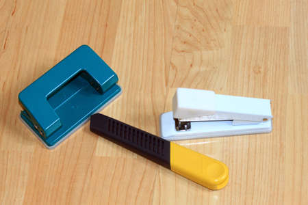 A photograph showing a stapler, a hole puncher and a paper cutting knife displayed on a wooden の写真素材