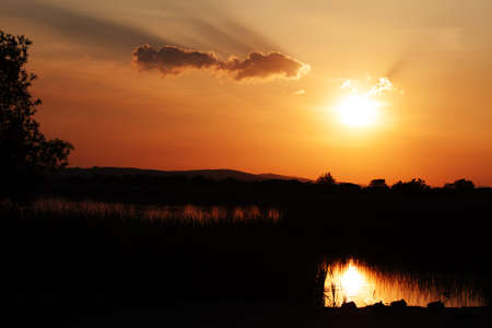 Itâs nearing sunset with a red sky.sunset, red, orange, yellow, silhouette, sky, clouds, trees, water, river, ducks, evening, black, white, summer, calm, peaceful, quiet, contemplative, inspiring, sunset, red, orange, yellow, silhouette, sky, clouds, trees, water, river, ducks, evening, black, white, summer, calm, peaceful, quiet, contemplative, inspiring,の写真素材