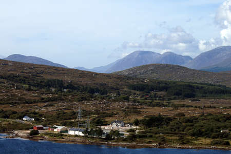 A very busy landscape with water, buildings, pylons, trees and mountainsの写真素材