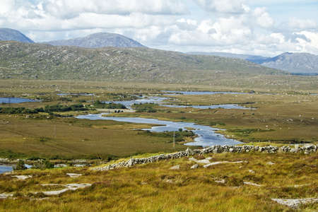 A landscape with mountains, meandering water and a stone wall.の写真素材