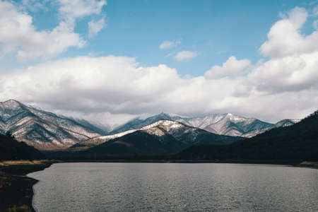 Mountain lake with snow-capped peaks under a blue cloudy skyの写真素材