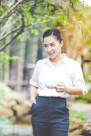 Businesswoman drinking coffee in the garden,She looked at the coffee mug and smiled happily.の写真素材