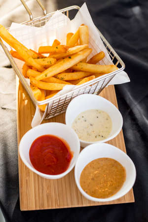 French fries in a metal basket with sauce on a wooden floor.