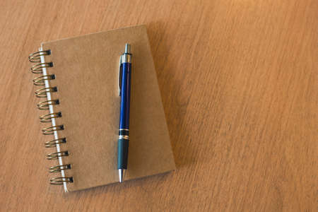 Brown notebook with pen on wooden deskの写真素材
