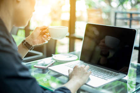 A woman works with a computer on the table with a phone, she picks coffee to drink. in the office.のeditorial素材