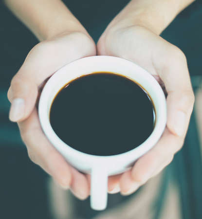 Woman's hand holding cup with coffee,heart-shaped.The concept of sending coffee with your heart.のeditorial素材